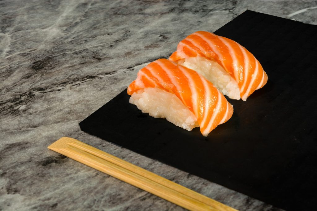 two pieces of sushi on a black plate with chopsticks